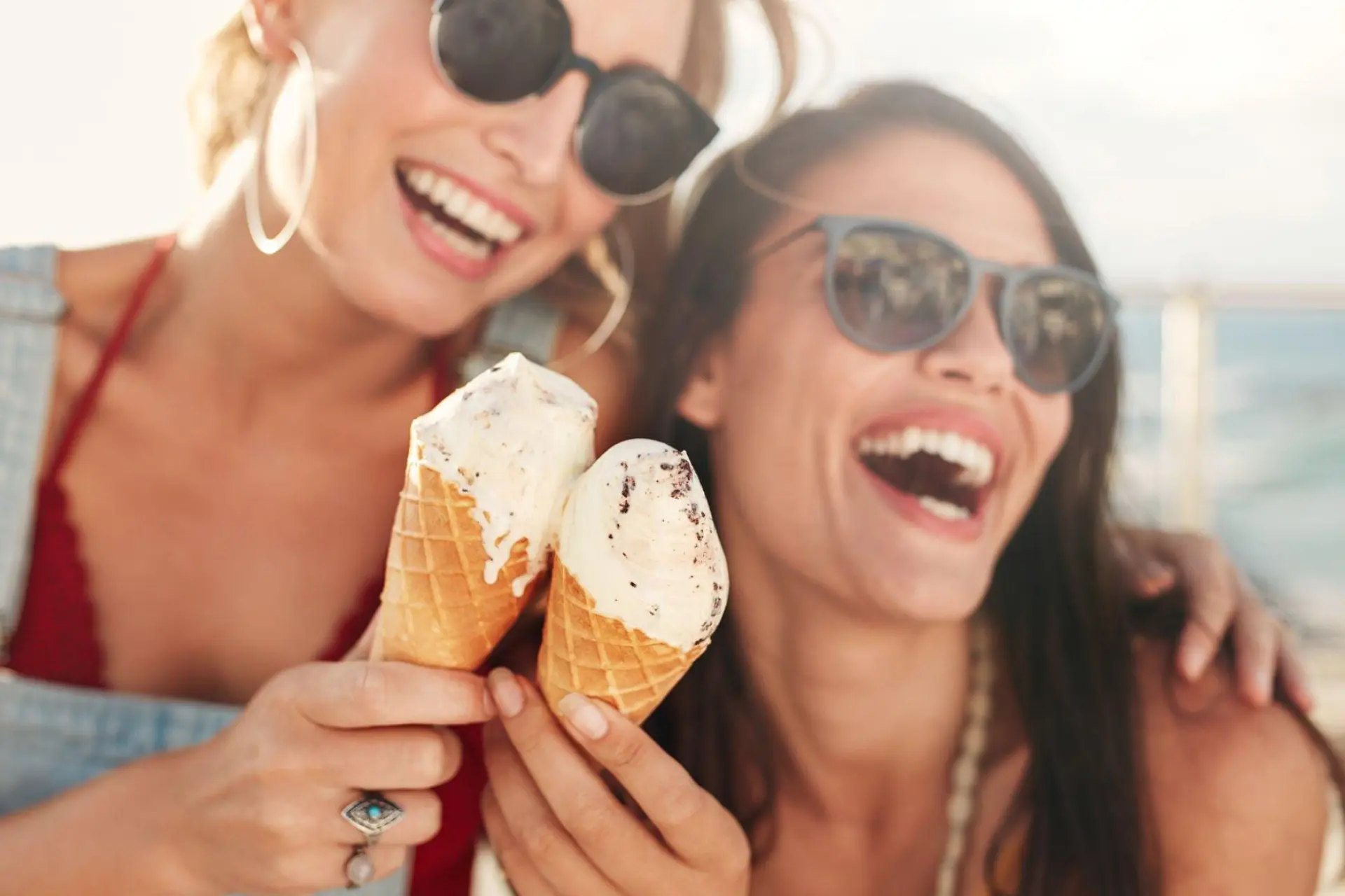 Receitas de sobremesas geladas: duas meninas tomando sorvete na praia e sorrindo.