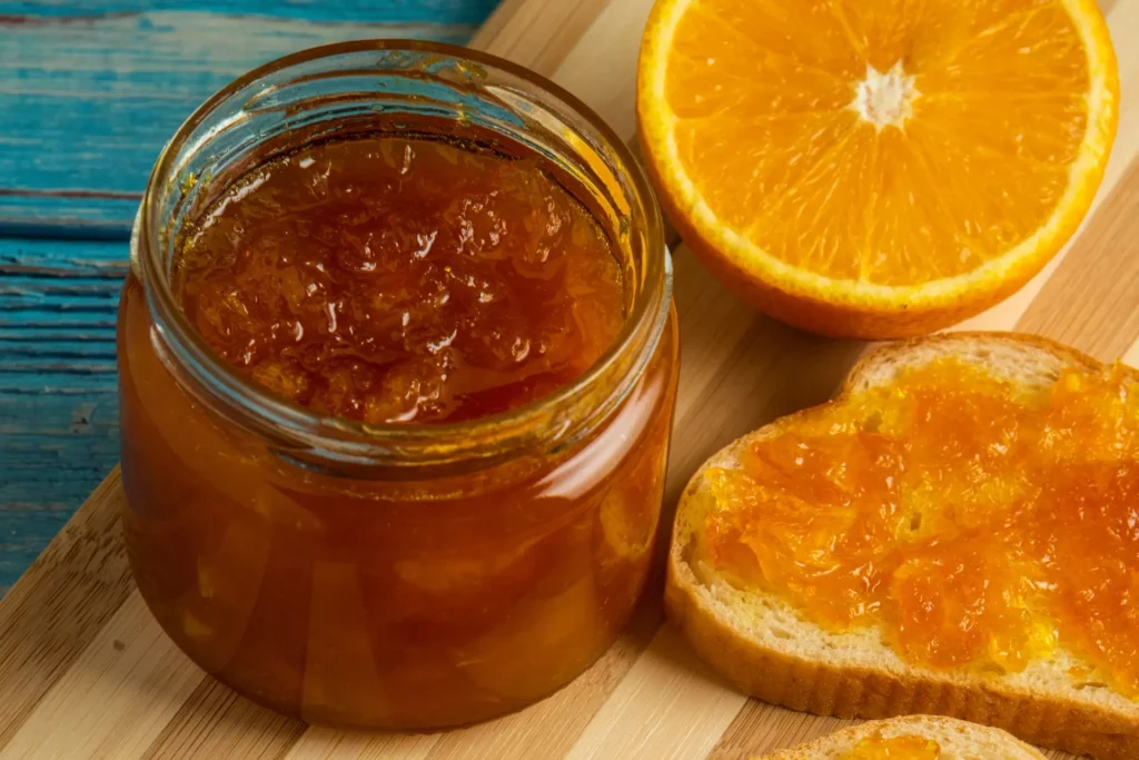 Geleia de laranja em um pote de vidro ao lado de uma laranja e pão