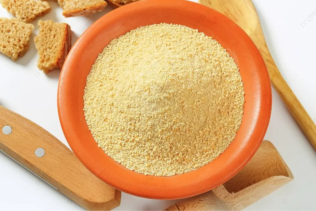 Farinha de rosca em um pote laranja com pães e utensílios de cozinha ao lado.